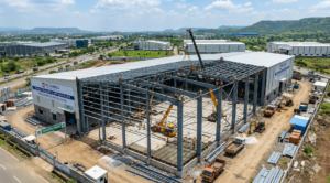 Aerial view of a large industrial warehouse construction project with steel structure installation, cranes, workers, and modern manufacturing units in an industrial park.
